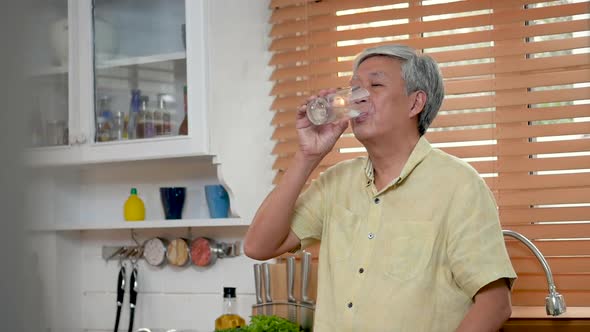 Portrait senior Asian man drinking water in the kitchen at home.