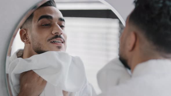 Male Reflection in Mirror 30s Indian Arabian Man with Beard in Bathroom After Washing Wipes Wet Face alt