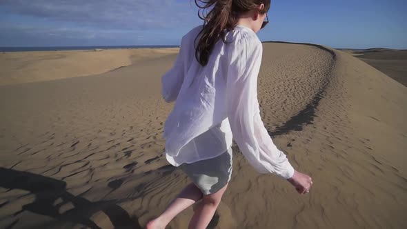 A Happy Woman in Casual Clothes Runs Along a High Dune in the Desert on the Shore of the Atlantic