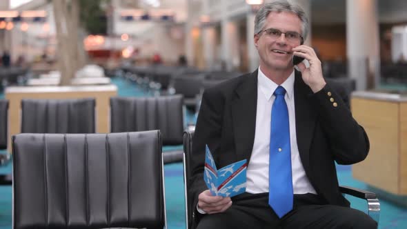 Mature business sits in airport lobby talking on cell phone alt