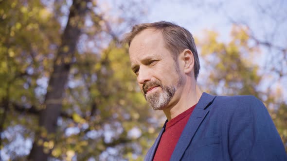 A Middleaged Handsome Caucasian Man Looks Around in a Park in Fall  Closeup From Below