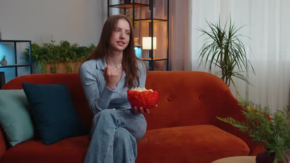Woman Sitting on Couch Eating Popcorn and Watching Interesting TV Serial Sport Game Online at Home alt