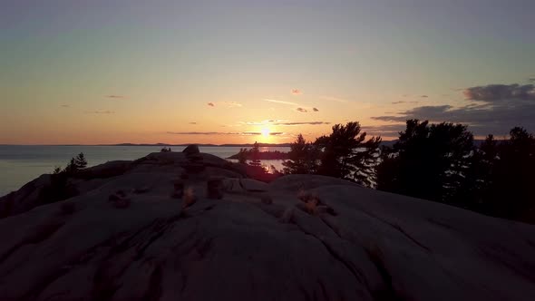 Reveal of Inukshuk on Rocky Pine Tree Island at Sunset, Drone Aerial Wide Dolly Out. View of Blue La alt