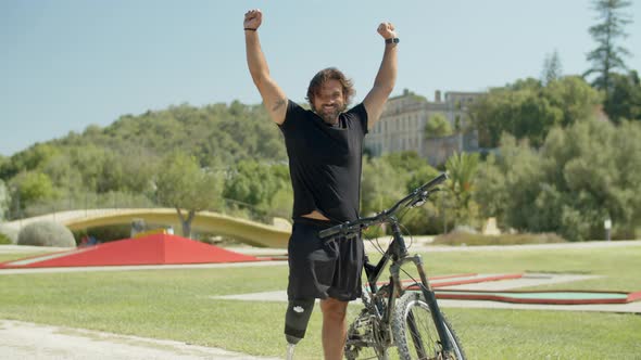 Happy Cyclist with Bionic Leg Raising Hands As Sign of Victory alt