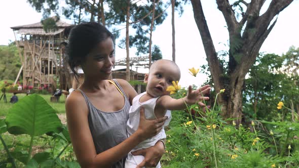 Adorable Baby and Mother Playing with the Flowers on Summer Day in the Garden