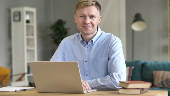 Smiling Businessman Looking at Camera While Working on Laptop alt