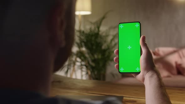 Handheld Camera Back View of Man Holding Chroma Key Green Screen Smartphone Watching Content Without alt