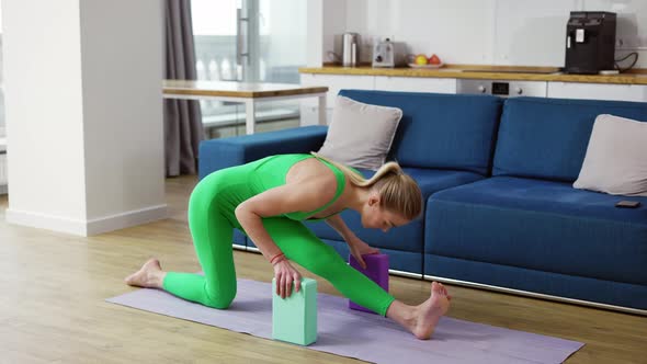Woman Stretching Legs with Yoga Blocks in Living Room at Home alt