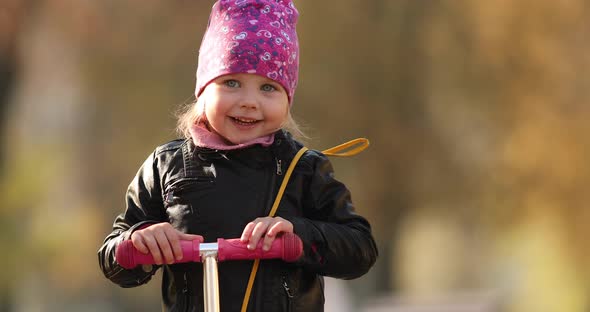 Cute Little Girl with a Scooter Waving at Camera