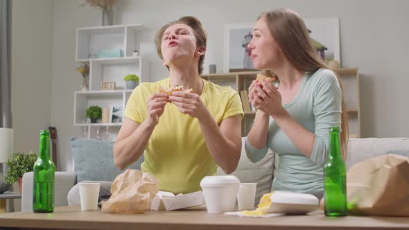 Young Couple Eating a Hamburger and Watching TV in the Living Room alt