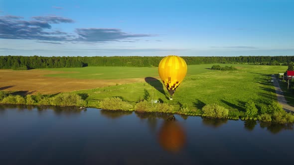 Yellow balloon rises slowly over river bank in ray of setting sun with aeronauts alt