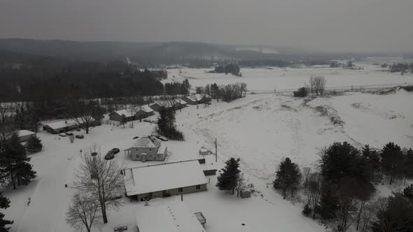 Aerial view of rural neighborhood in snow covered valley.  Cloudy sky and mountains in distance.