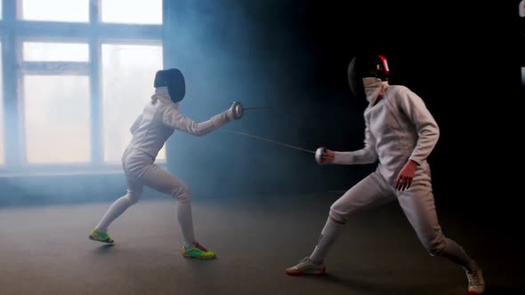 Two Young Women Fencers Having a Training Duel in the Studio alt