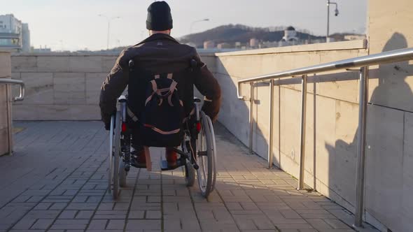 Adult Man in Wheelchair is Using Handicapped Ramp in Modern City for Moving alt