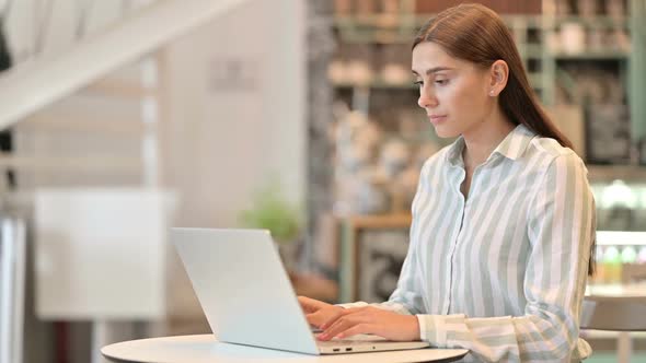 Beautiful Young Latin Woman Celebrating Success on Laptop in Cafe alt