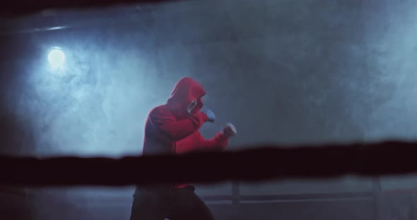 Young Male Fighter is Practicing Punches in the Ring a Dark Hall with Tubers of Smoke alt