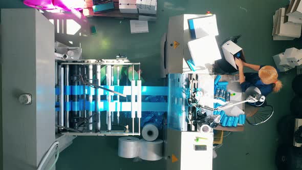 Female Worker Packing Blue Plastic Bags From a Production Line Into a Box alt