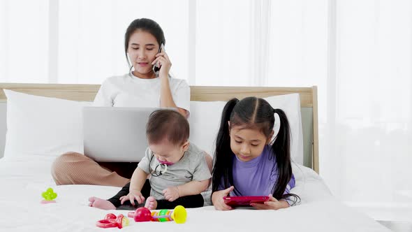 Baby and little daughter play toy on bed while Busy freelancer mother working on laptop