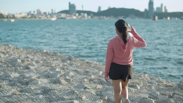 Fitness female holding a water bottle walking on the rock at the seaside.
