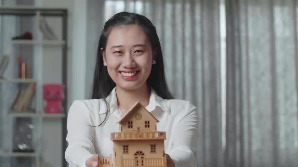 Close Up Of Asian Woman Smiling And Showing House Model To Camera In The New House alt