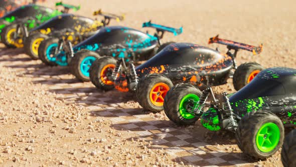 Multiple colourful remote-controlled buggy cars on start line in the desert. alt