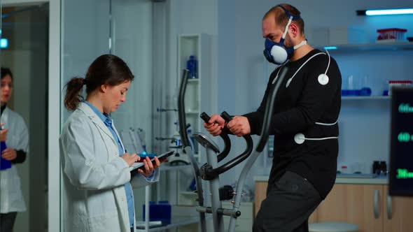 Doctor Asking Patient About His Health While Sportsman Running on Cross Trainer alt