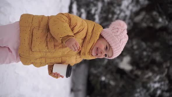 Child Girl Drinking Cocoa and Eating Cookie Outdoors in Winter Snowy Day alt