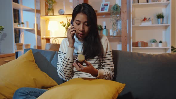 Asian woman hold medicine sit on couch use smart phone to consult with doctor at home night.