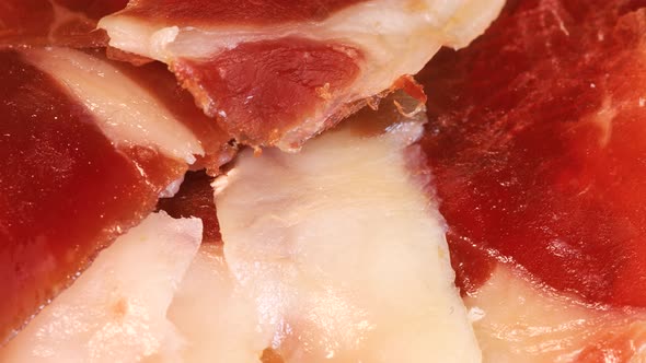 Slices of intense spanish serrano ham with bread rotating on wooden board, close up view from above. alt