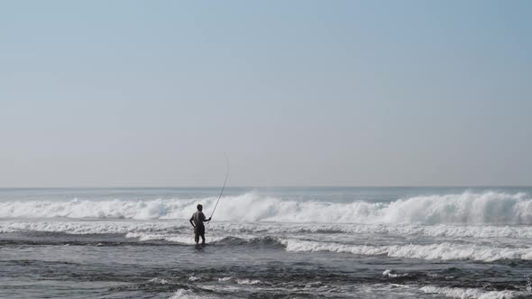 Local Fisherman Holds Rod in Hand in Waving Blue Ocean alt