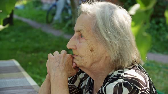 an Old Woman Sitting in the Garden Hands in Front of Her Face She Looks Forward Thoughtfully and