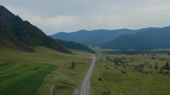 Traffic cars on asphalt road between green field and mountains in Altai