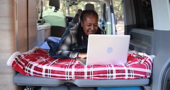 Mature african woman using computer laptop inside mini van camper alt