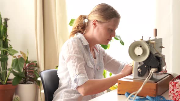 Work at Home. Young Blonde Woman Sews on a Typewriter in a Bright Room