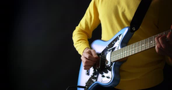 Male Guitarist in a Yellow Jumper Plays an Electric Guitar on Black Background alt