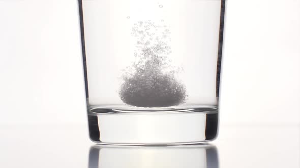 An effervescent tablet falls on a bottom of a clear glass