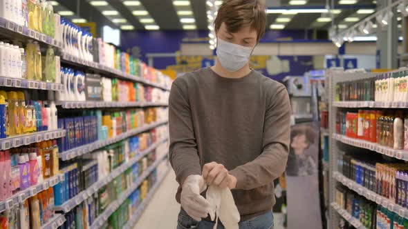 Coronavirus Pandemic Protection. Man in a Medical Mask Puts on Rubber Gloves in a Supermarket alt