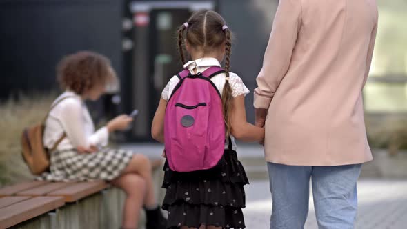 An Adult Woman Leads Her Little Daughter By the Hand to School alt