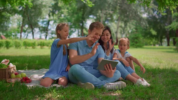 Smiling Family Waving Hands Communicate Using Tablet on Nature in Summer Day alt