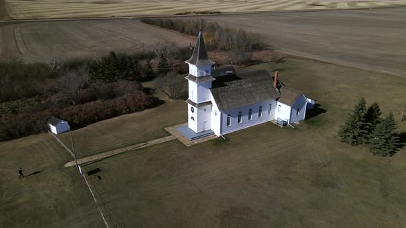 Drone orbiting around old country church in Alberta's prairies while slowly ascending and revealing alt