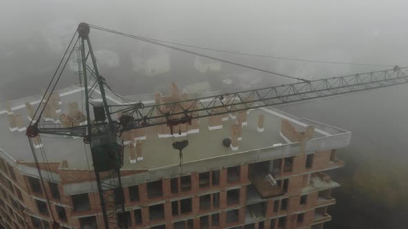 Birds eye view on tower crane in fog standing next to residential building. 