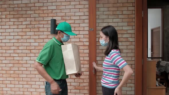 Delivery man with face mask gives parcel to an Asian woman. alt