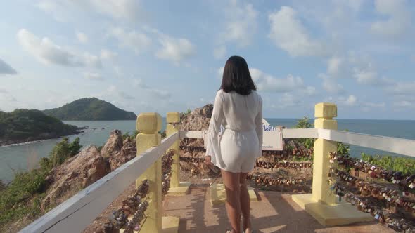 A women wearing a white outfit walks to the end of a rocky lookout and looks out over a bay with isl alt