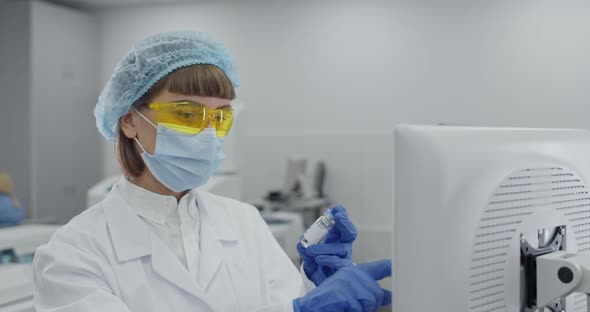 Female Medical Worker in Protective Mask and Googles Entering Data on Computer alt