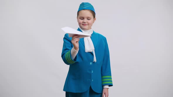 Cute Girl in Air Hostess Uniform Playing Landing Paper Plane Turning to Camera Smiling alt
