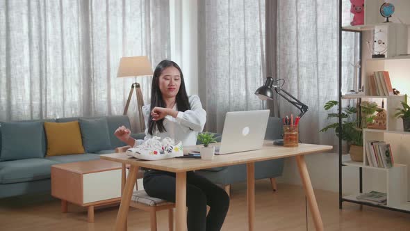 Asian Female Footwear Designer Stretching After Working On A Laptop At Home alt