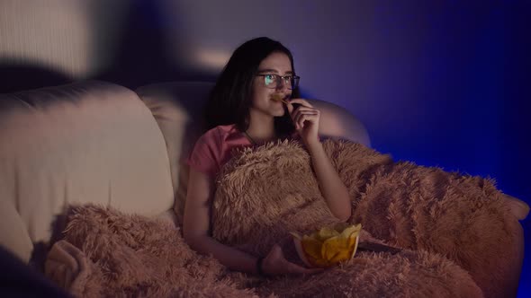Pretty Brunette Girl with Glasses Eating Potato Chips and Watching Tv at Home