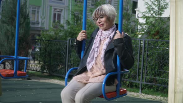 Portrait of Happy Senior Woman Swinging on Swings in Sunshine Outdoors Smiling alt