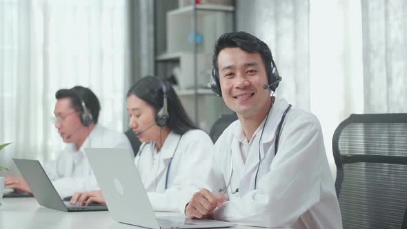 A Man Of Three Asian Doctors With Stethoscope Working As Call Centre Agent Smiling To Camera alt