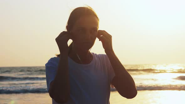 Woman is Putting Earphones to Listen Music Before Jogging on the Sea Beach